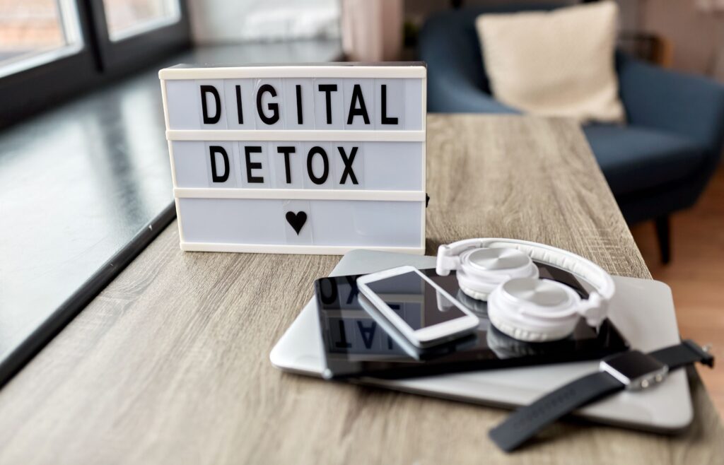 Tabla z napisom "Digitalni detox" ob pametnih napravah na mizi.